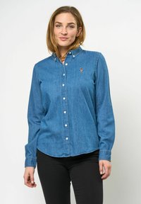 Denim button-up shirt in lichtblauw met een kraag, lange mouwen en een klein geborduurd detail op de borst. Glad oppervlak.