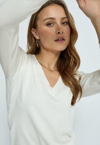 Balts, viegls adīts džemperis ar V-veida kakla izgriezumu un garām piedurknēm. Gluda tekstūra, brīva piegriezuma, ar smalkiem izšuvumiem.