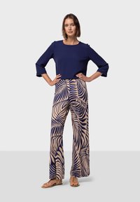 Haut bleu marine à manches trois-quarts associé à un pantalon large arborant un motif de feuilles de palmier beige et bleu foncé. Sandales dorées.
