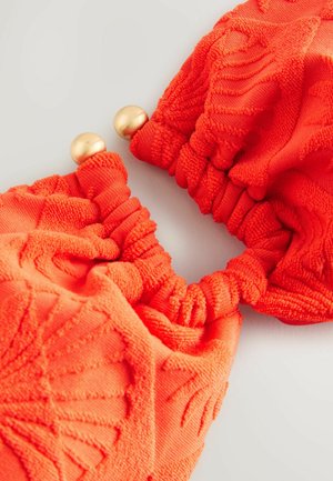 Orange textured hair scrunchie with gathered fabric design, featuring two metallic gold spherical accents at the joining point.