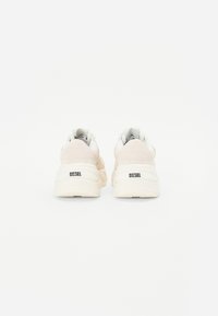Sneakerid, mis on valmistatud pehmest beežist ja valgest materjalist, paksude tallaga, ümmarguse kujuga ning "DIESEL" brändinguga kannal.