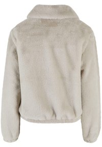Lys beige faux fur jakke, med krave, lange ærmer og en samlet kant. Blød tekstur med et hyggeligt udseende. Ingen synlige lukninger.