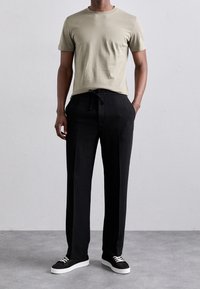 Beżowa bawełniana koszulka połączona z czarnymi spodniami na sznurek. Spodnie mają luźny krój i są noszone z czarnymi trampkami.