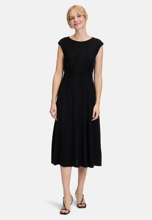 Zwarte, mouwloze midi-jurk met een ronde halslijn en een uitlopende rok. Gemaakt van zachte stof met een gladde textuur. Minimalistisch ontwerp en pasvorm.