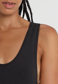 Svart ribbad linne med djup rundad halsringning och breda axelremmar, som visar en slät textur och en figursydd design.