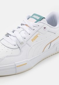 Vit lädersneaker med texturerade paneler, med guld- och turkos accenter, rund tå, platta snören och gummisula.
