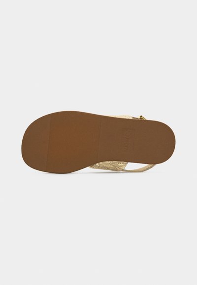 Φλατ σανδάλι με καφέ υφή στη σόλα και ανοιχτό μπεζ πλεγμένους ιμάντες, εμφανιζόμενο από κάτω σε απλό φόντο.