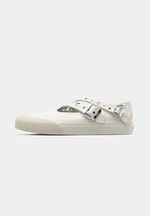 Canvas slip-on shoe in off-white featuring a cut-out design, metallic buckle accents, and a ridged rubber sole. Minimalist design elements.