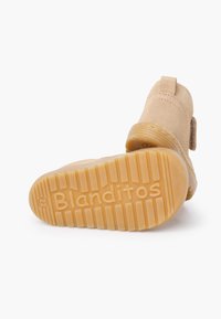 Botín de ante color cuero con suela de goma que presenta ranuras horizontales y el nombre de la marca "Blanditos" en relieve en la parte inferior.