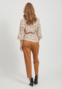 Blouse crème à motifs floraux avec des manches évasées, assortie à un pantalon marron fuselé et des chaussures à talons noires. Vue de dos.