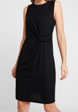 Robe noire sans manches longueur genou avec un détail de nœud torsadé à la taille sur une personne sur un fond uni.