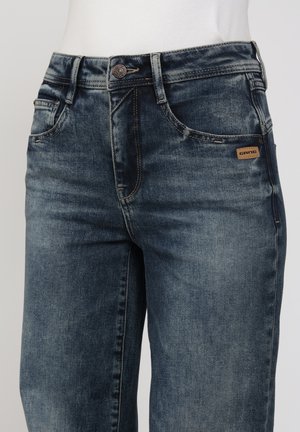 Verblasste schwarz-blaue Jeans aus Denim mit Fronttaschen, Gürtelschlaufen, Knopfverschluss und kleinem braunem Logoaufnäher an der rechten Tasche.