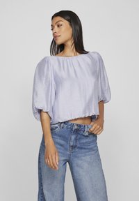 Top lila deschis, din satin, cu un decolteu lat și pliat, și mâneci bufante, asociat cu blugi din denim de culoare albastru deschis, cu talie înaltă.