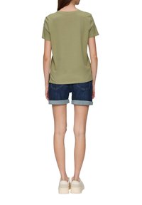 Olijfgroen kortekoushemd gecombineerd met donkere spijkerbroekshorts met omgeslagen onderkant, gedragen met lichtgekleurde platform sneakers.