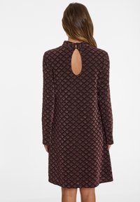 Long-sleeve dress in dark burgundy, textured with a diamond pattern, featuring a keyhole opening at the back and subtle sheen.