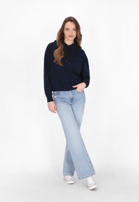 Hanorac scurt navy cu siret, asociat cu blugi evazați de culoare albastru deschis și adidași albi. Texturi netede, laico, și detalii subtile cu logo.