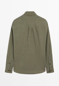 Koszula z długim rękawem w oliwkowym kolorze, z kołnierzem na guziki, fakturowaną tkaniną oraz plisą z tyłu zapewniającą większą swobodę ruchów i elastyczność.