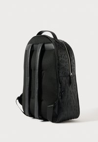 Μαύρο δερμάτινο σακίδιο με ανάγλυφο κείμενο, πλέγμα με μαξιλάρι στην πλάτη, δύο ρυθμιζόμενους ιμάντες ώμου και επάνω χερούλι σε λευκό φόντο.