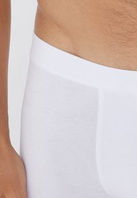 Bóxer de algodón blanco con una textura suave y cintura elástica, que presenta un diseño simple y una silueta ajustada.