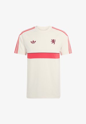 Camiseta blanca de Adidas con una franja horizontal roja, tres rayas rojas en las mangas y los logotipos de Adidas y un león en color granate en el pecho.