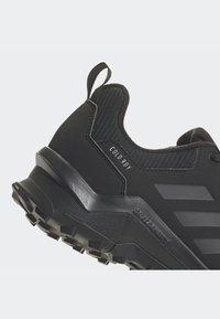 Zapato deportivo negro con parte superior texturizada, puntera reforzada y marca en contraste. Presenta una suela resistente y antideslizante para mayor tracción.