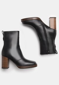Stivali alla caviglia in pelle nera con punta arrotondata, tacco a blocco in texture legno, zip laterale e linguetta. Texture liscia con dettagli di cucitura minimi.