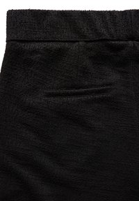 Tessuto nero strutturato con una finitura morbida e ad anelli. Presenta una cintura larga e una piccola tasca posteriore discreta.
