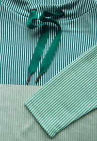 Gestreepte stoffen kleding met groene en lichtblauwe lijnen. Heeft een trekkoord halslijn met zilveren accenten en een brede mouw.