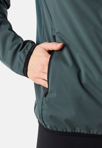 Veste vert foncé avec une finition lisse et mate. Dotée d'une poche zippée sur le côté et d'un détail en noir au niveau des poignets. Matériau léger.