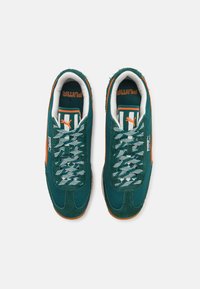 Adidași din daim verde cu detalii din plasă, având accente portocalii, o talpă texturată și sireturi cu model. Logo-ul PUMA afișat proeminent.