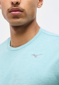 Κοντινό πλάνο ενός ατόμου που φοράει ανοιχτό μπλε μπλουζάκι με στρογγυλή λαιμόκοψη και μικρό γκρι λογότυπο στην αριστερή πλευρά του στήθους.