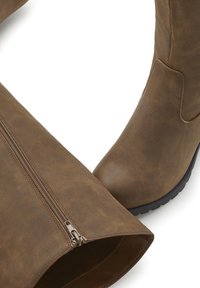 Knee-high boot ruskea tekonahasta, jossa on sivuvetoketju ja teksturoidut pinnat, pyöreä kärki ja musta kumipohja.