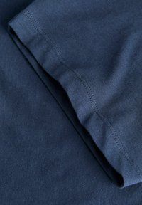 Gros plan d’un tissu bleu marine montrant une couture détaillée sur le bord plié d’une manche de vêtement en coton.