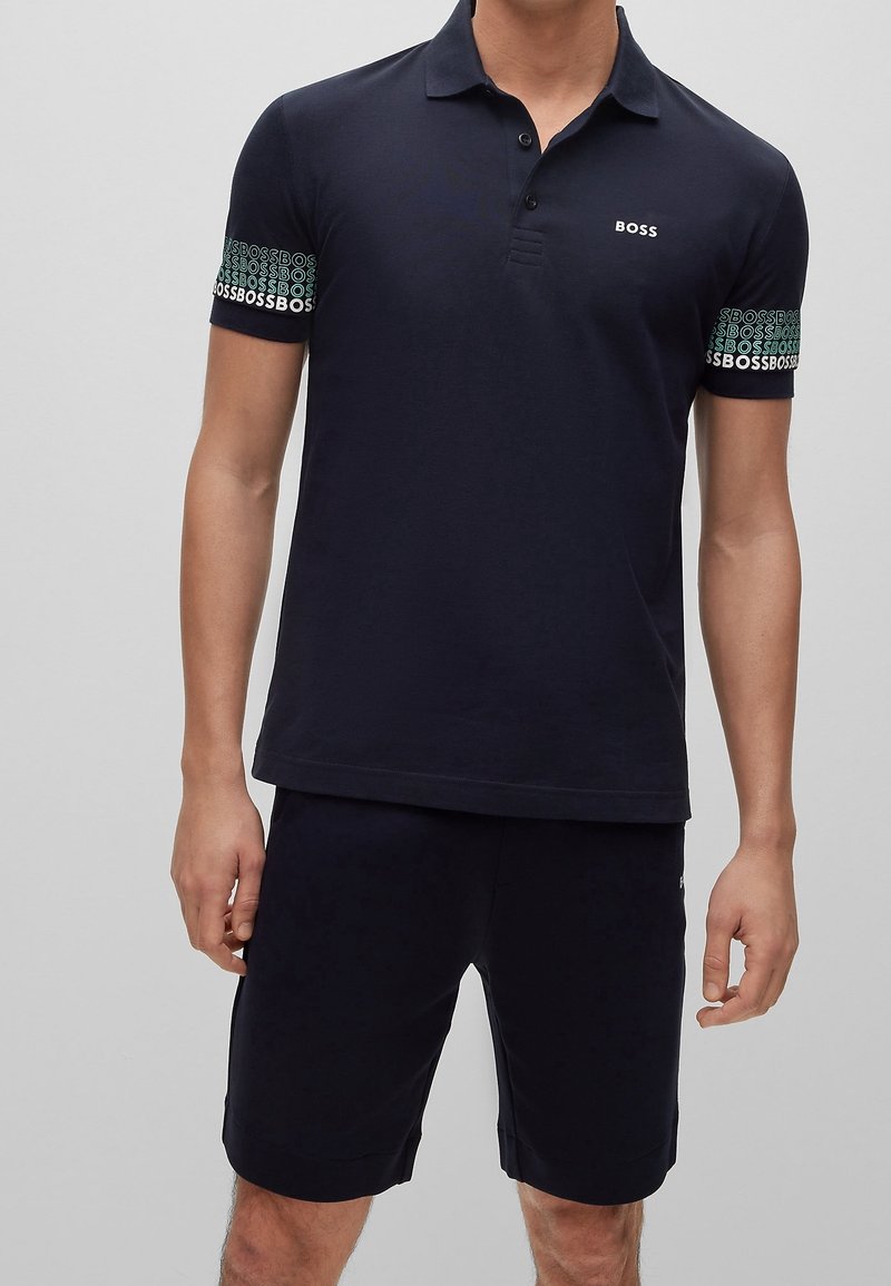 Polo shirt bleu marine avec un col à trois boutons, manches texturées arborant un motif "BOSS", accompagné de shorts assortis.