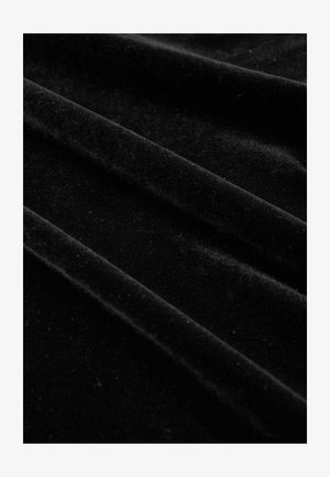 Tela de terciopelo negro con una textura suave y lisa, que presenta pliegues drapeados que generan sutiles reflejos de luz y un color rico y profundo.