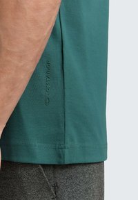 Zielona bawełniana koszulka z krótkim rękawem, z fakturowanym wykończeniem i delikatnym nadrukiem logo na bocznej szwie.