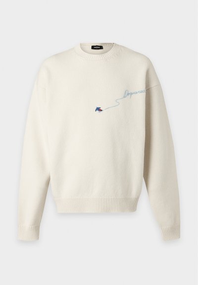 Pull en maille couleur crème avec poignets et ourlet côtelés, orné de petits oiseaux brodés bleu et rouge et d'un texte en cursive bleu clair sur la poitrine.