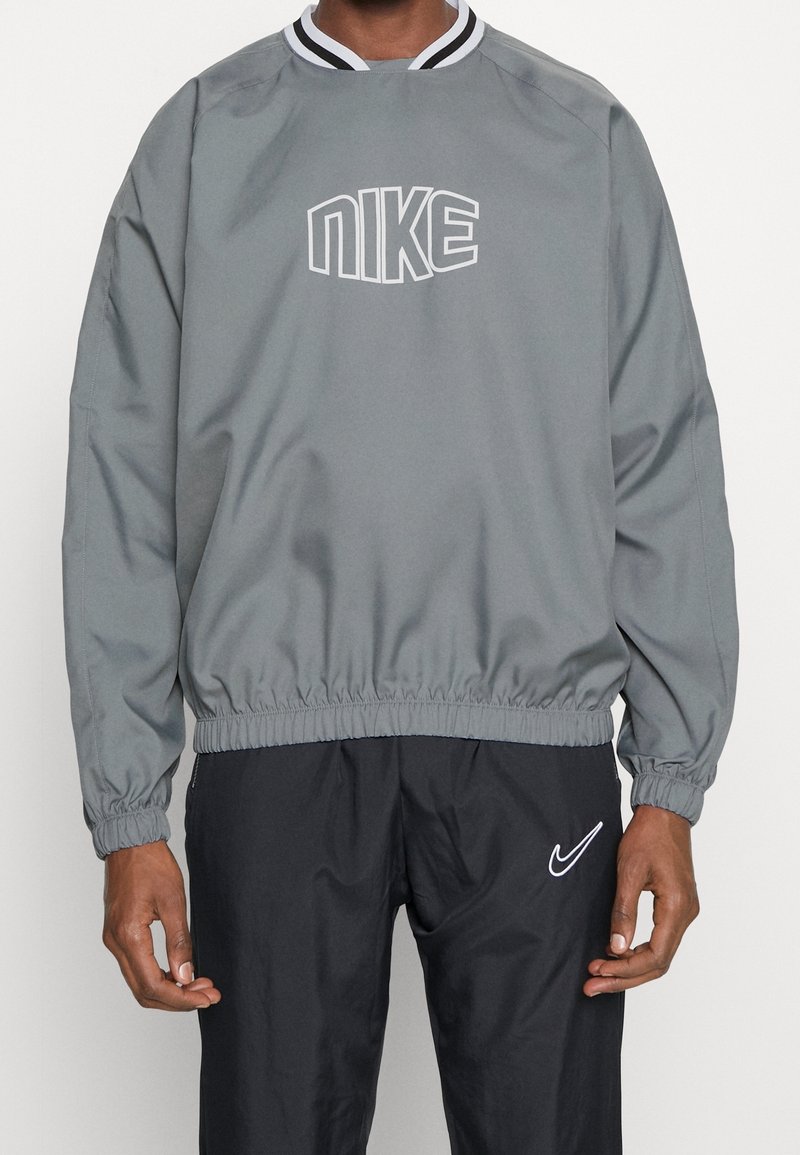 Pullover grigio Nike con cintura ed elastico ai polsi, caratterizzato da logo bianco sul petto e colletto a righe bianche e nere. Materiale morbido e liscio.