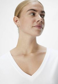 Camiseta blanca de cuello en V con una textura suave y lisa, que presenta un escote redondeado y costuras limpias y suaves a lo largo de los bordes.
