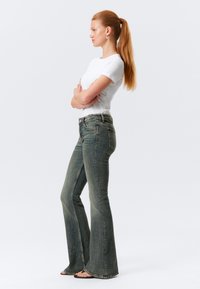 Jeans dzwonowate w oliwkowej deninie, z wysokim stanem, kieszeniami z przodu i schludnym wykończeniem u dołu. Zestawione z dopasowaną białą koszulką.