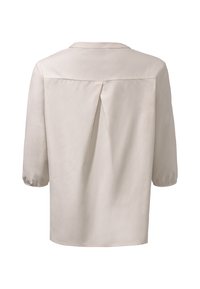 Blouse beige avec manches 3/4 élastiquées et un pli creux inversé à l'arrière sous un empiècement, vue de dos sur un fond blanc.