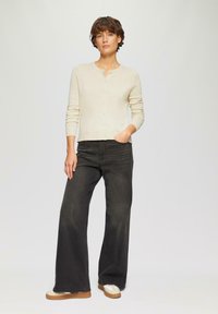Cardigan en tricot crème avec un devant boutonné, assorti à un jean noir à jambes larges. Les détails remarquables incluent des manches longues et une coupe décontractée.