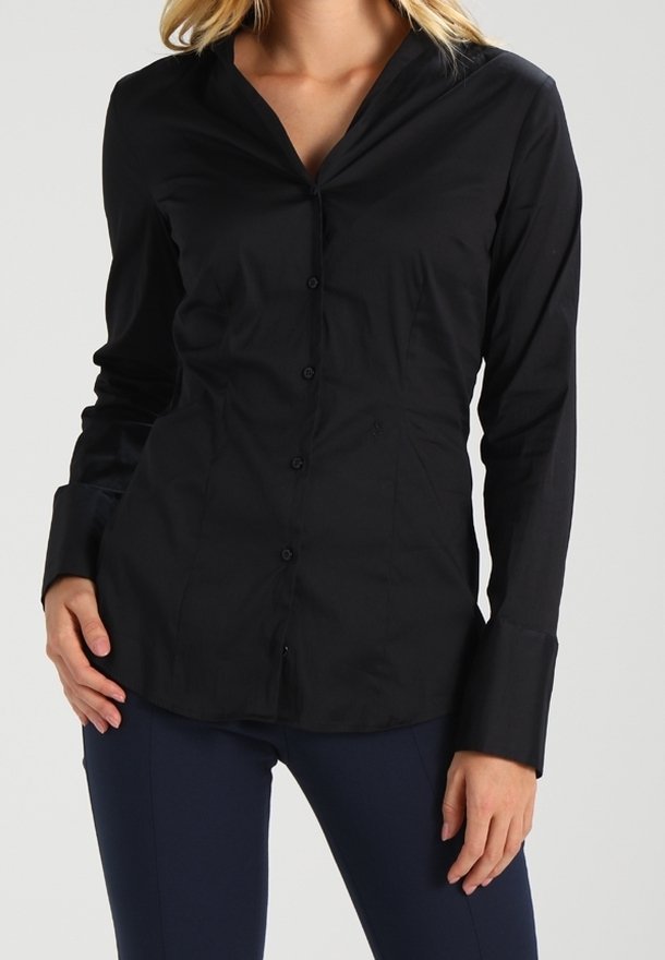 Chemise noire à manches longues avec un col pointu, dotée d'un design ajusté, d'une texture lisse et de boutons visibles sur le devant.