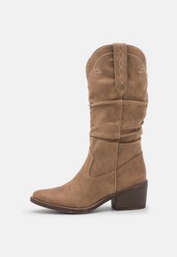 Botas de cowboy de ante marrón con un diseño arrugado, punta afilada y tacón apilado. Costuras decorativas a lo largo de la parte superior y acentos laterales.