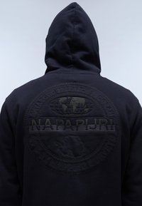 Marineblauwe hoodie met een groot, ton-sur-ton geborduurd logo op de achterkant, met een wereldbolontwerp en de tekst "NAPAPIJRI" in verhoogde stiksels.
