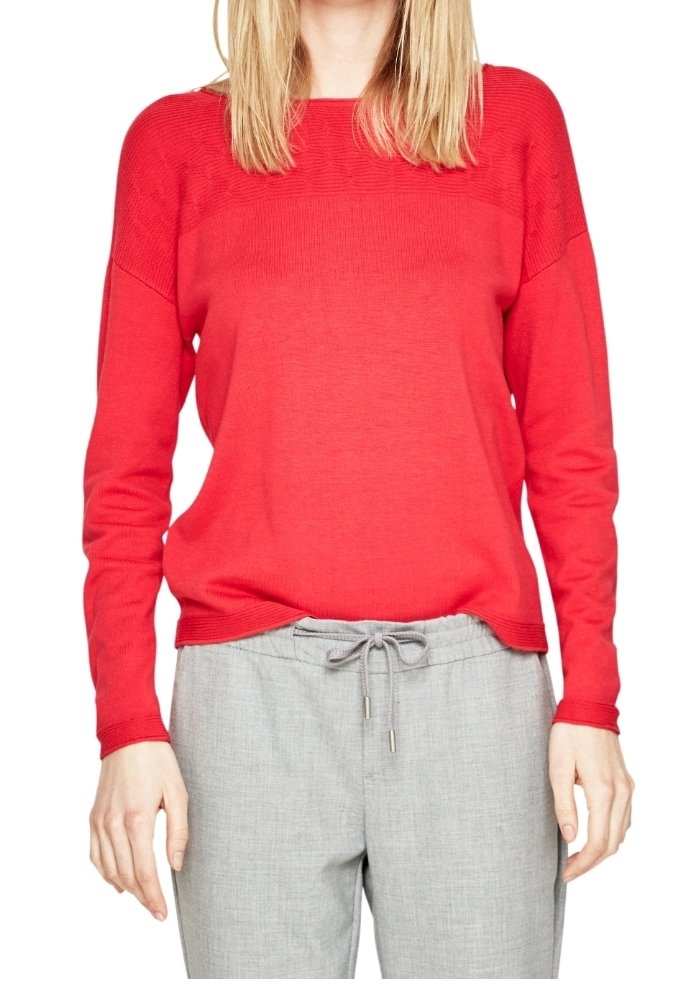 Pull en maille rouge à coupe décontractée, col côtelé et manches longues, associé à un pantalon gris clair à enfiler avec une taille élastiquée et un cordon de serrage.