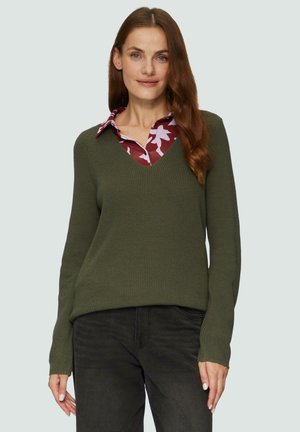 Olivgrüner Strickpullover mit V-Ausschnitt, kombiniert mit einem bordeauxfarbenen gemusterten Hemd darunter, vor einem hellen Hintergrund.