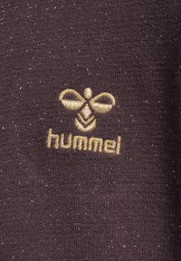 Svart texturerad tyg med guld broderad bi-logotyp och "hummel"-text. Materialet har subtila glittrande detaljer genom hela.