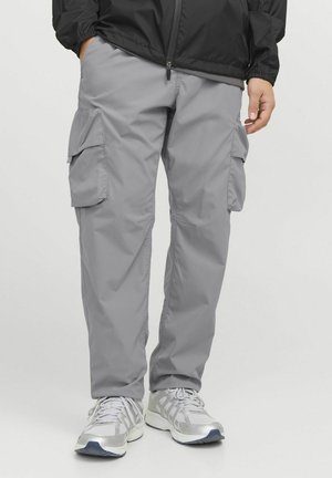 Pantalons cargo gris en tissu léger, dotés de plusieurs poches latérales et d'une coupe décontractée. Associés à des chaussures de sport argentées.