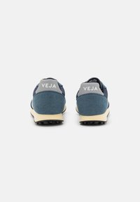 Navy blue sneakers with grey accents, featuring a suede and mesh upper, flat cream outsole, and prominent "VEJA" logo on the heel.